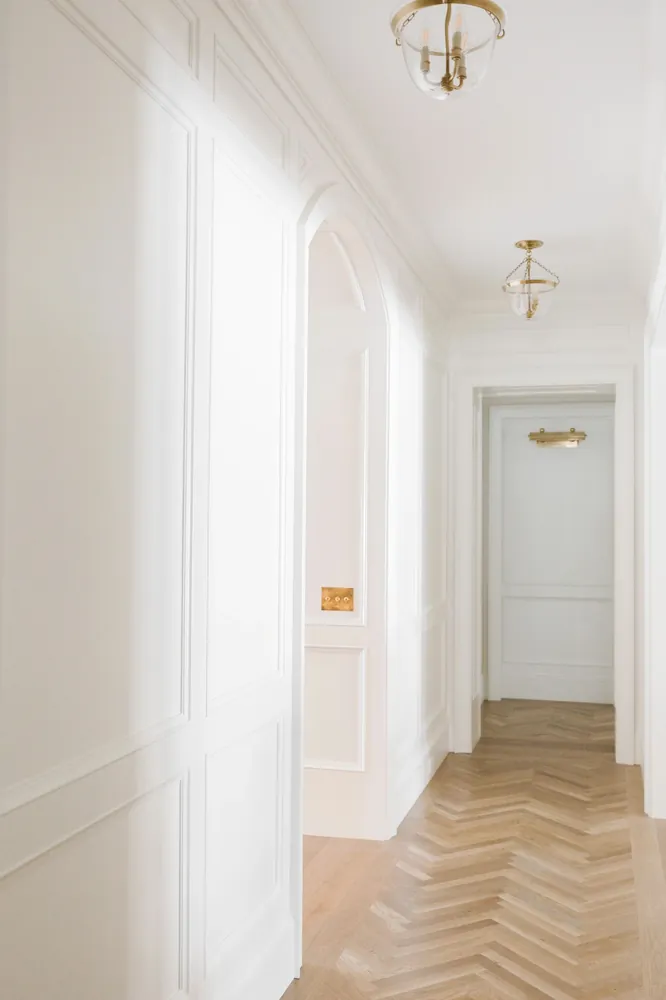 A hallway with white paneling and a herringbone wood floor