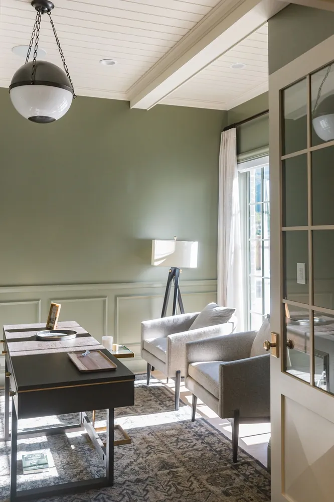 A study with sage green walls, paneling and a glass-paned door